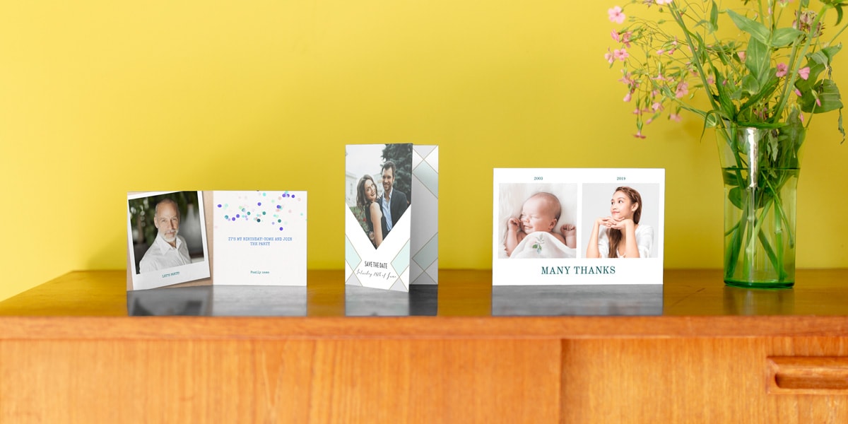Trois cartes personnalisées avec photo sur une petite table en bois devant un mur jaune.