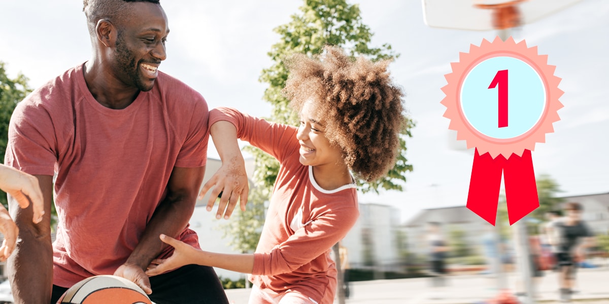 Un homme et sa fille jouant au basket-ball en extérieur par beau temps. La mise au point est sur le premier plan, l'arrière-plan est flou.