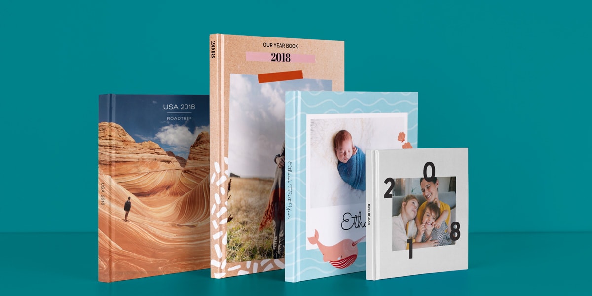 Selectie van 2018 jaarboeken tegen een petrolkleurige achtergrond, inclusief een reisboek van een roadtrip door Amerika, een jaarboek met een lichtbruine kaft, een babyboek en een klein fotoboekje met een witte kaft en een gezinsfoto op de voorkant