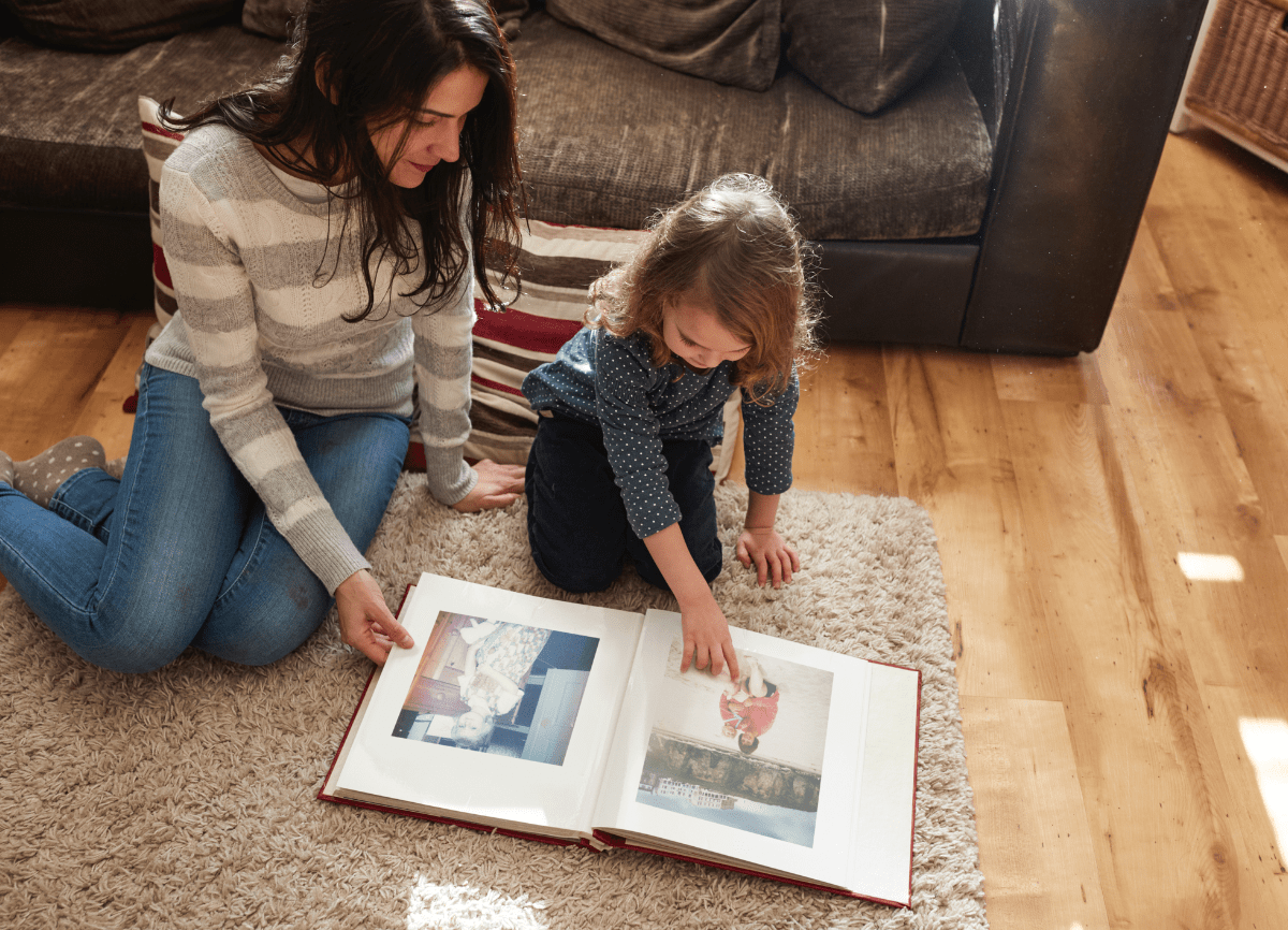 Een vrouw en een dochter die een oud fotoalbum op de woonkamervloer bekijken. 