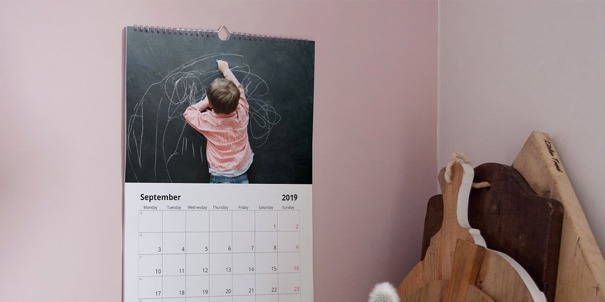 Een afbeelding van een fotokalender aan een roze muur, met een foto van een jongetje dat op een schoolbord tekent.