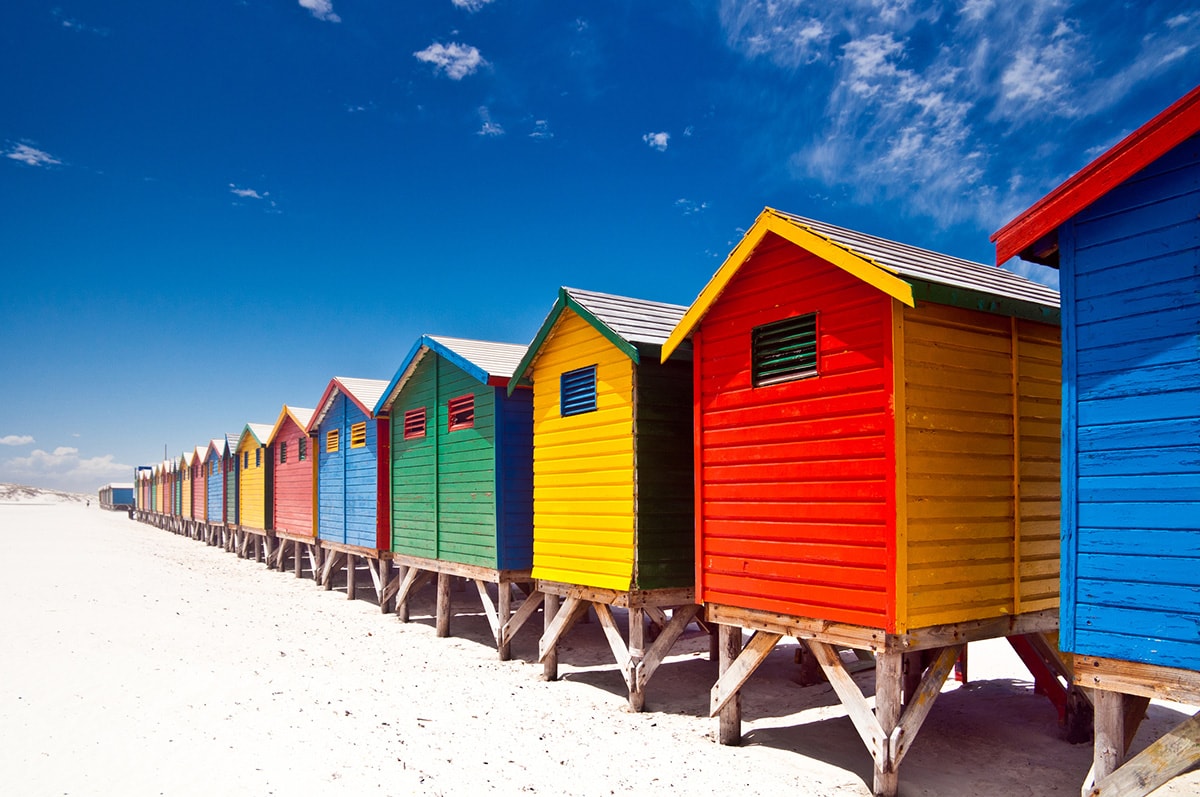 Een foto van een rij kleurrijke strandhutten op een zonnige dag.