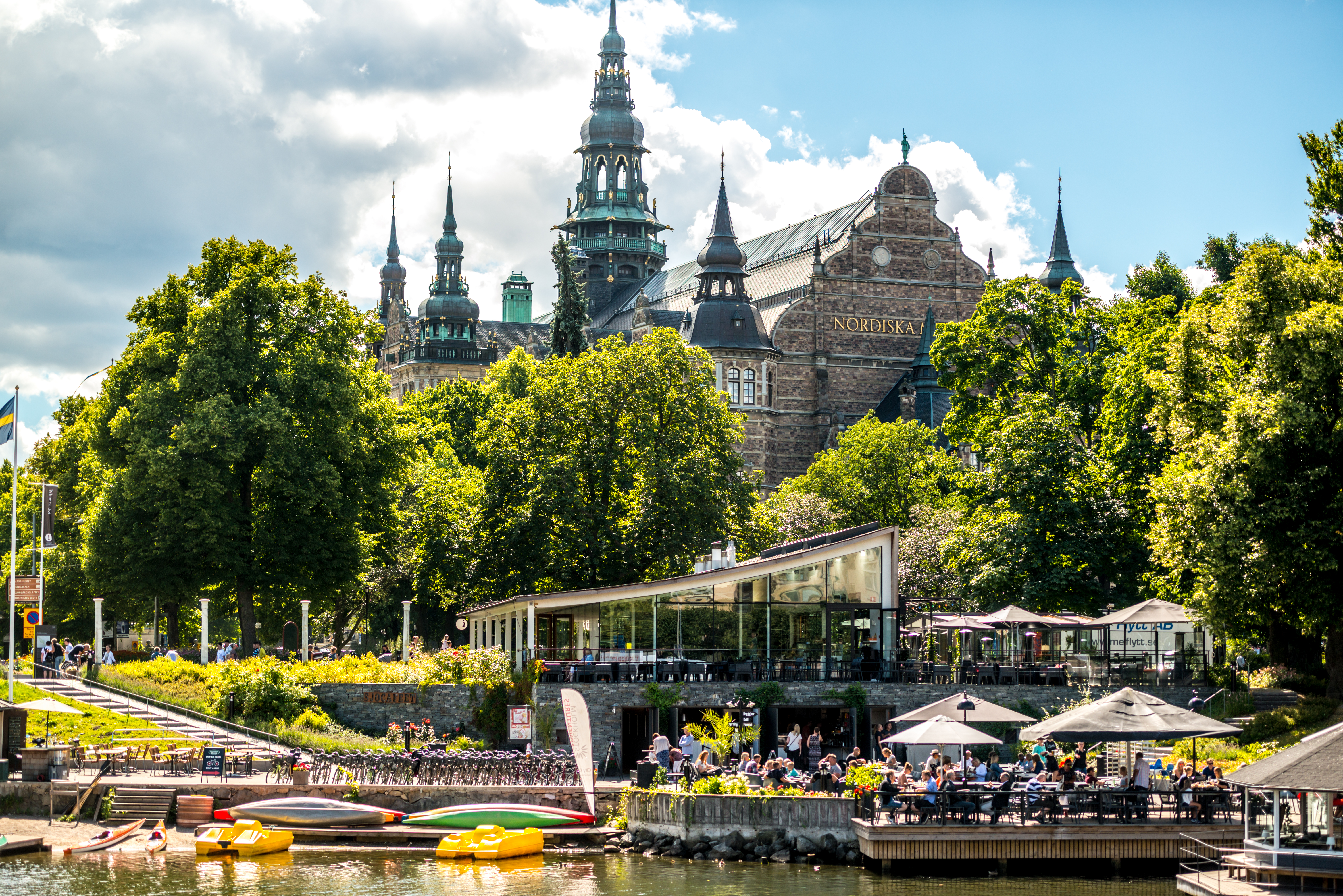 A photo of the Nordiska building in Stockholm, with a café in front, taken by the water’s edge. 