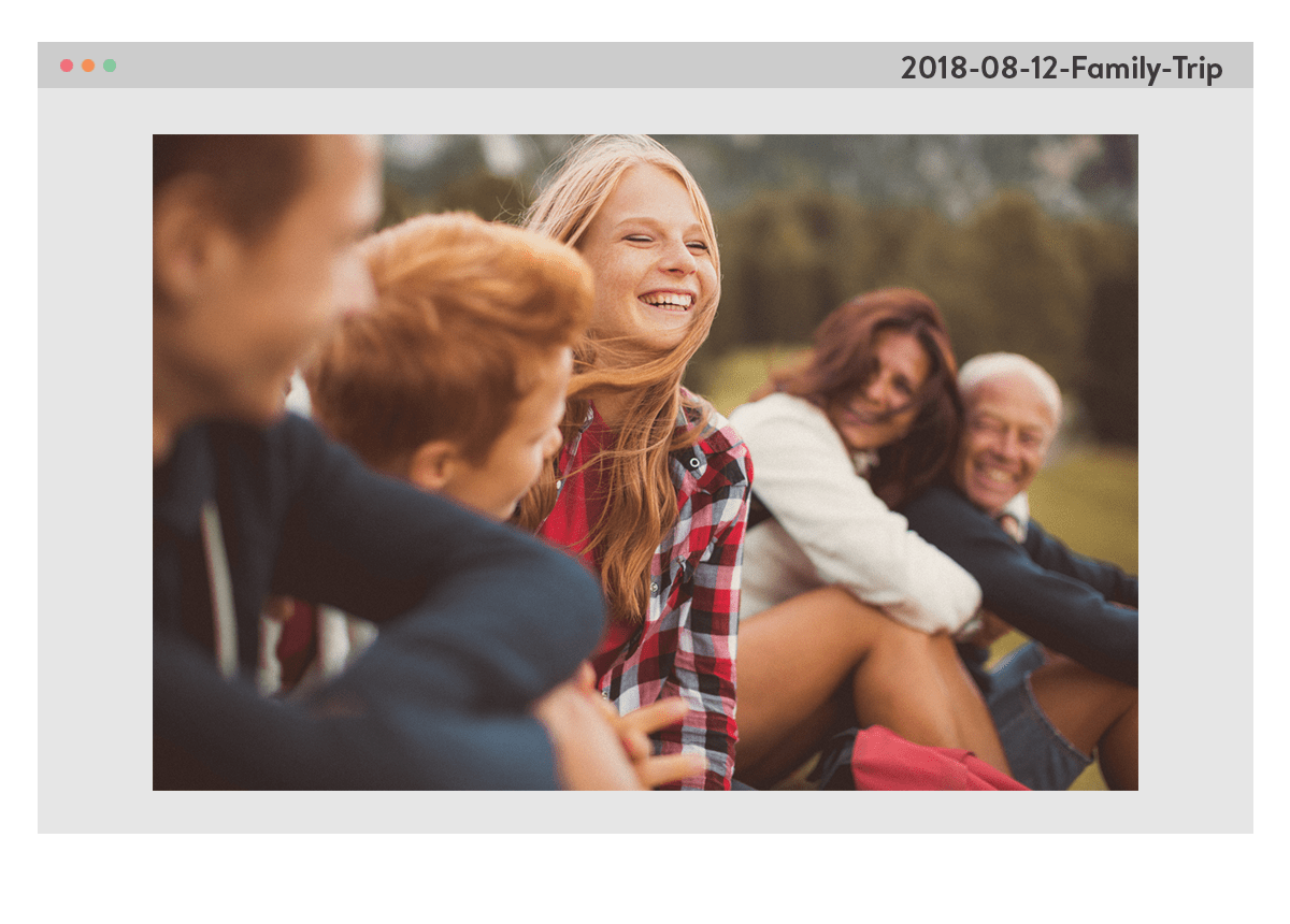 Una foto di una famiglia, seduta fuori sull'erba, sorridente. La foto è incorniciata da una finestra del computer, con il nome del file 2018-08-12-Family-Trip nell'angolo in alto a destra.