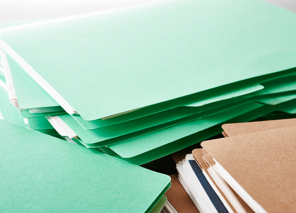 Three stacks of paper folders, two piles are green folders and the other stack is of brown folders.