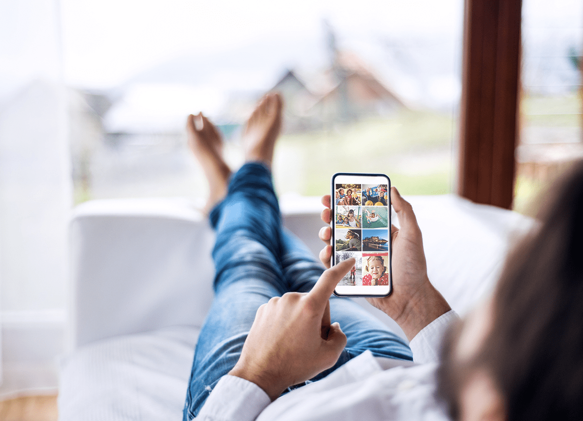  Un hombre acostado en un sofá blanco, hojeando fotos en su teléfono.