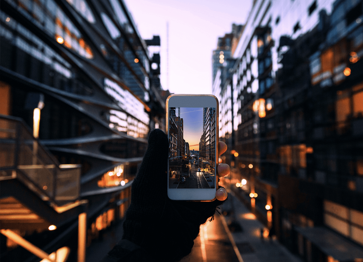 Someone taking a picture of a street at night with a white smartphone. The scene is blurred, but the image on the phone is in focus.