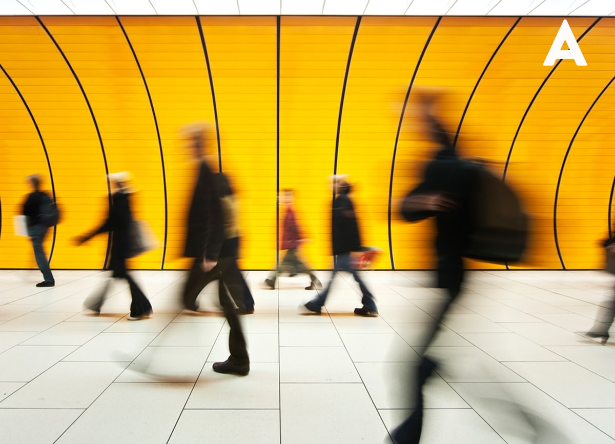 A blurred photo of a fast-moving crowd walking in a subway, with a bright orange lit-up background.