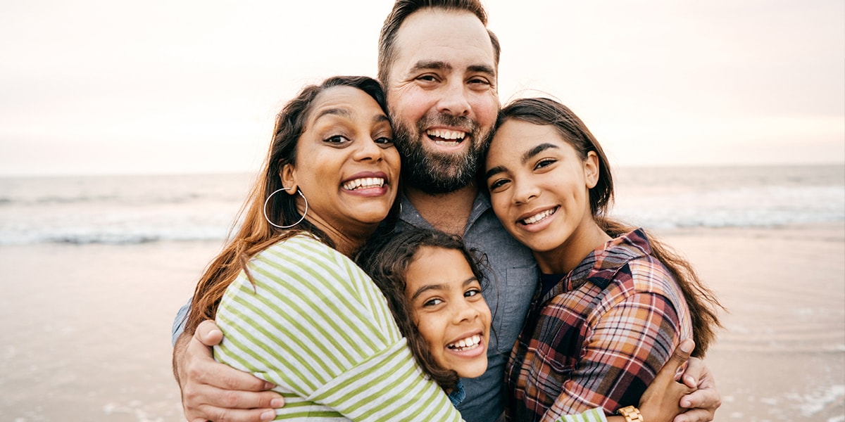 A photo of a family hugging on a beach at sunset.