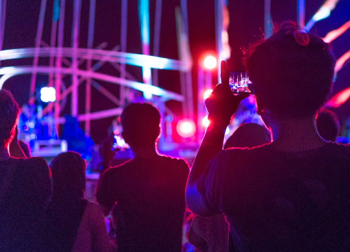 An image of people in a crowd at a concert. The lighting is low, and everything in the background, including the stage, is out of focus.