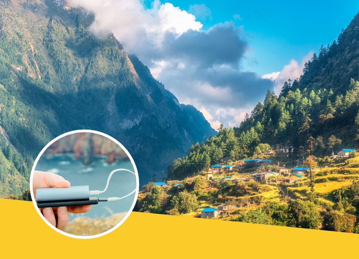 A beautiful shot of a mountain valley, with a small village in the background and pine tress covering the landscape, and a phone and power bank being held in front of a coastline within the roundel. 