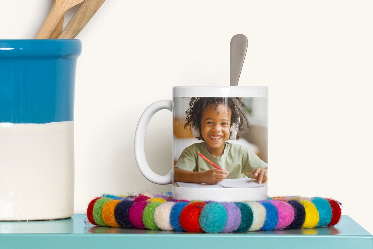 A photo mug with a picture of a little girl smiling sits on top of a colourful coaster.