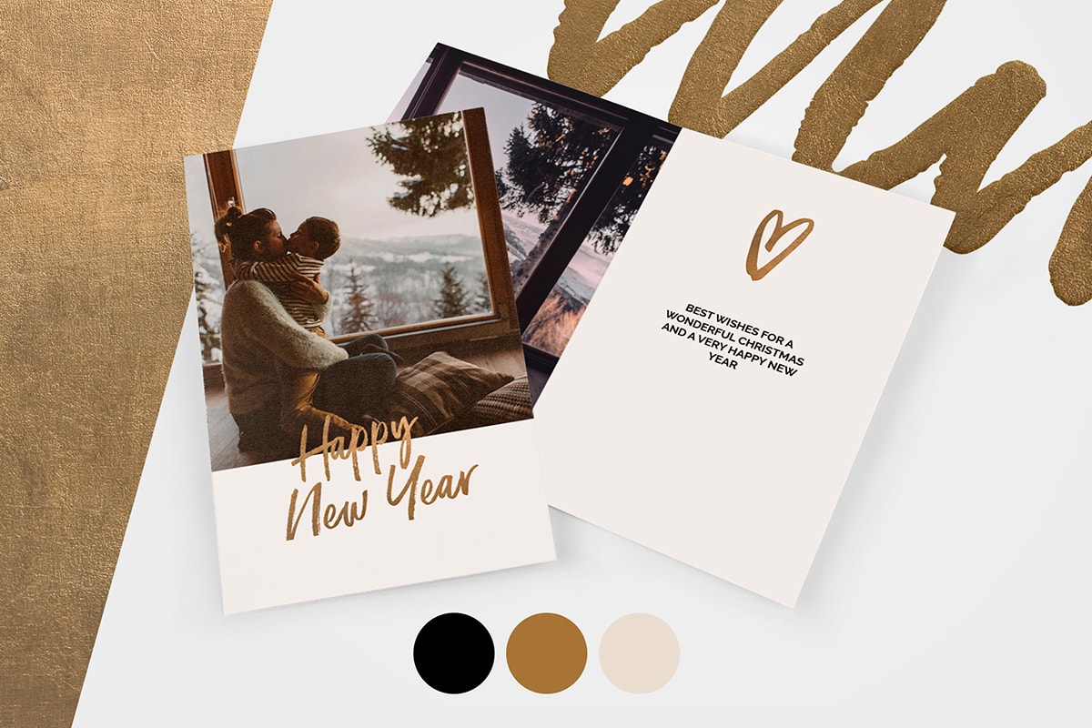 A personalised photo card with ‘Happy New Year’ written in gold script on the front. There’s a second copy open behind it with a metallic gold heart and a message on the page. The cards are on a pale grey background with metallic gold colour blocks, colour swatches, and a metallic swirly pattern in the corner.