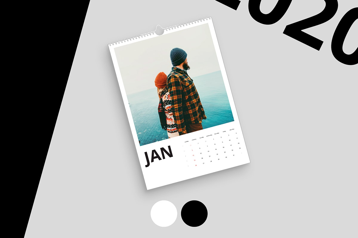 A personalisA photo calendar with a picture on the front of a young couple in plaid shirts, jumpers, and woolley hats stanging by the sea. The calendar’s on a pale grey background with black and white colour swatches and black typography in the corner. ed photo card with a multi-photo grid on the front and multi-coloured lettering. There’s a second copy open behind it. The cards are on a pale grey background with three colour swatches below, a teal colour block on the left, and colourful typography in the top right corner.