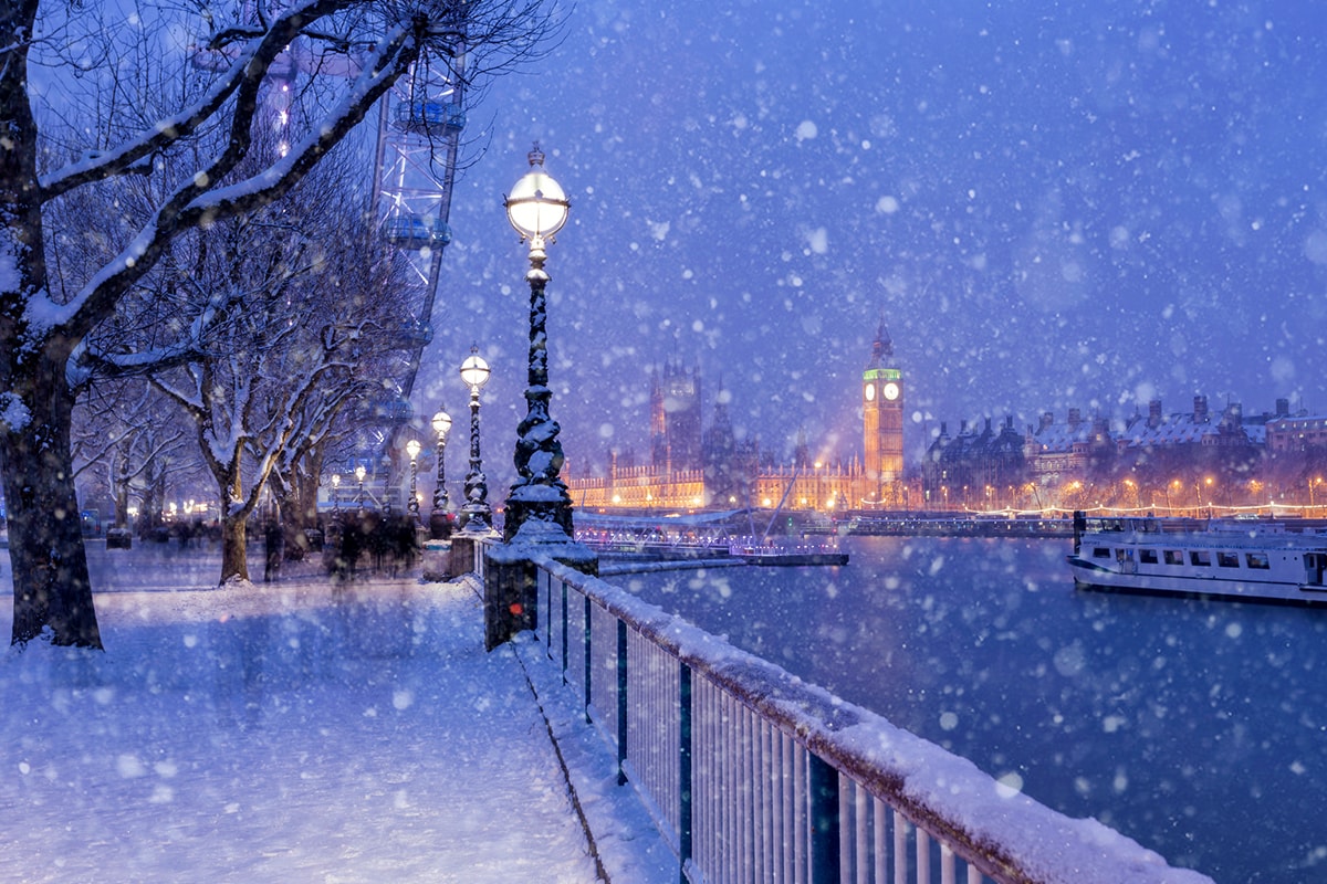 Ein Foto von London bei Nacht und Schneefall mit dem leicht verschwommenen Big Ben im Hintergrund und dem London Eye in der linken Ecke.