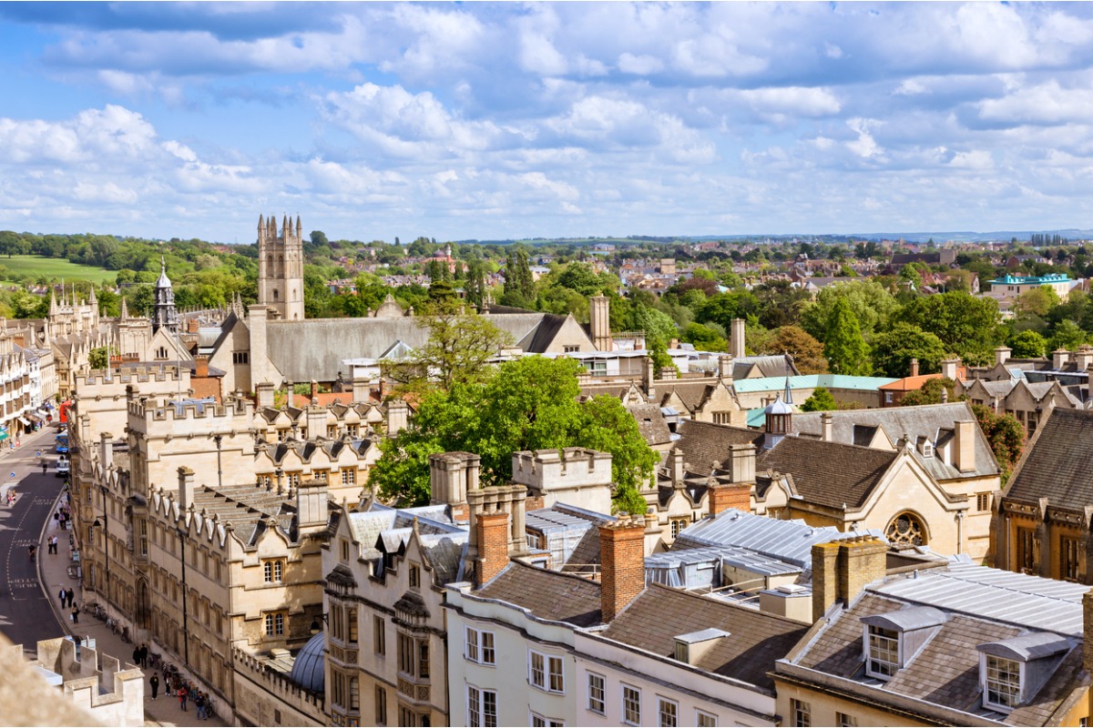Ein Foto der Dächer von Oxford und dem Glockenturm der Kathedrale. In der Ferne sind Bäume und Hügel zu sehen.