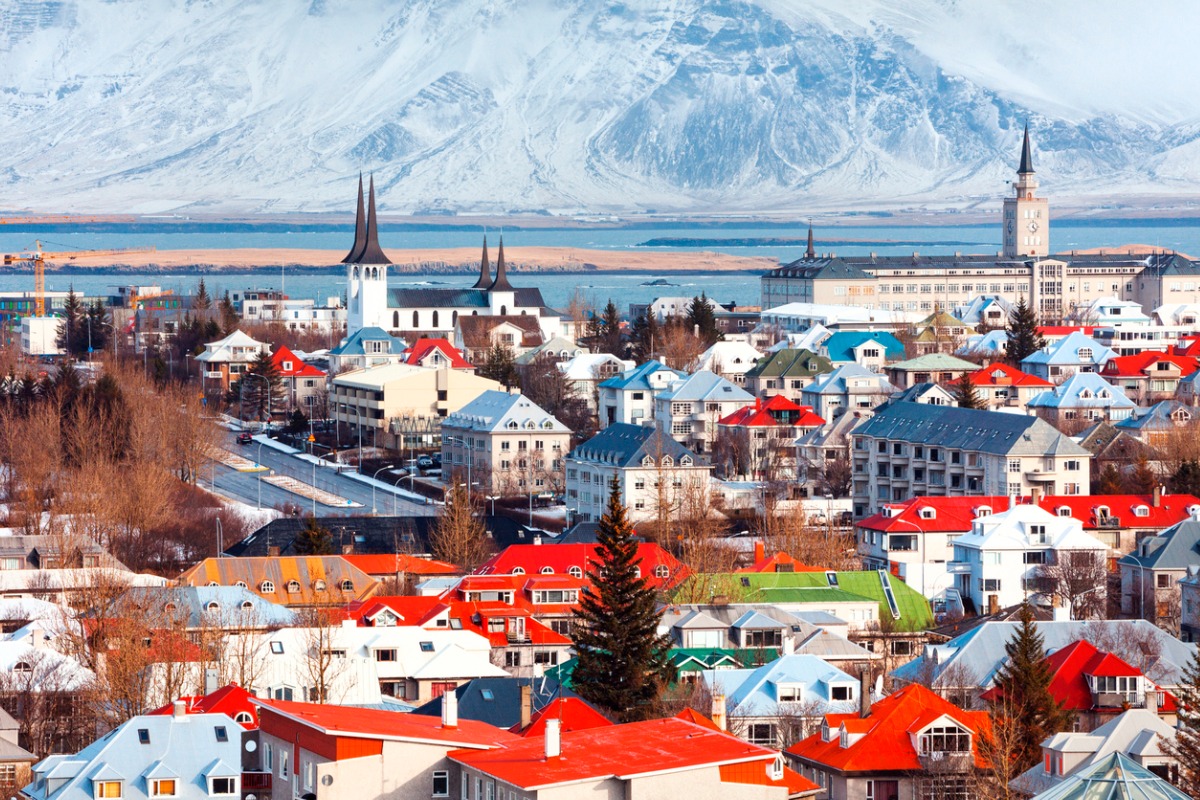 Ein Foto der bunten Dächer von Reykjavik. Im Hintergrund ist das Wasser und in der Ferne ein verschneiter Berg zu sehen.