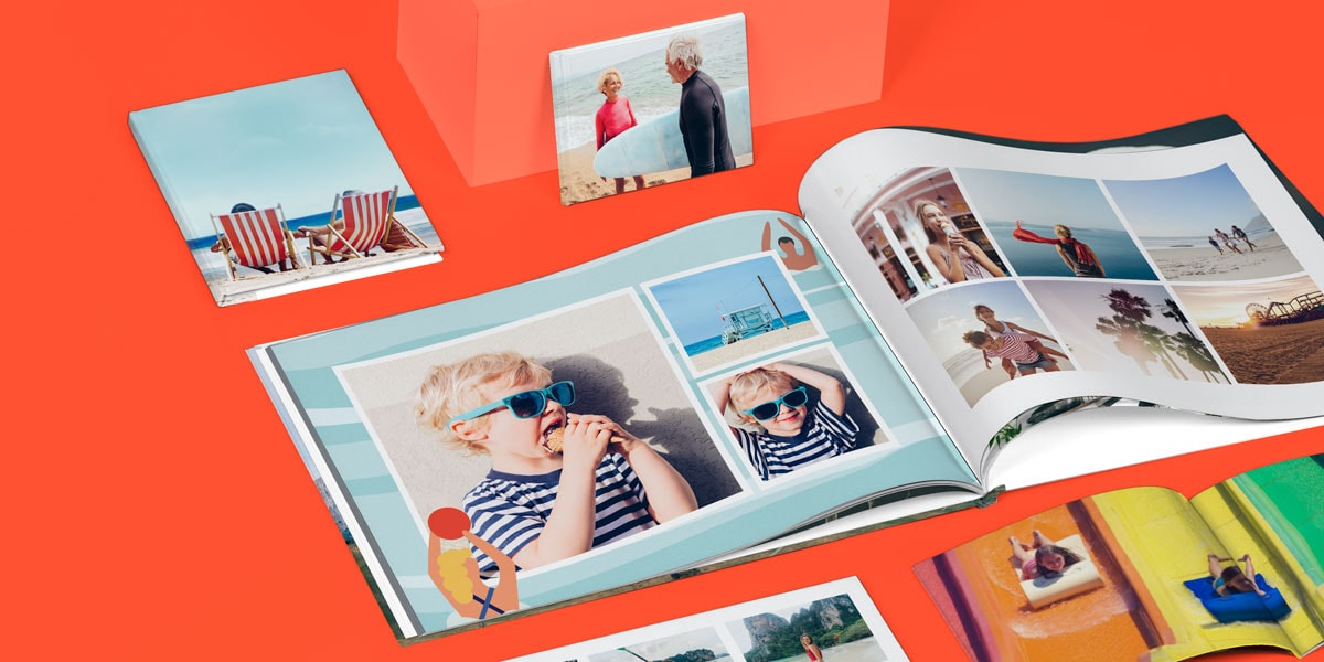 Eine Auswahl von fünf Fotobüchern, die aufgeschlagen auf einer hellen orangenen Oberfläche liegen und sommerliche Fotos zeigen.