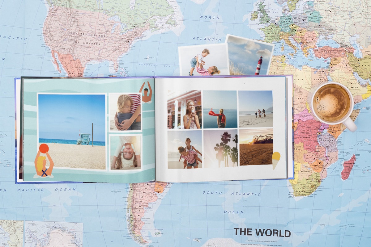 Ein vorgefertigtes Sommerfotobuch, das aufgeschlagen auf einer Karte liegt. Neben dem Buch befindet sich eine Tasse Kaffee und hinter dem Fotobuch versteckte Sommerfotos.