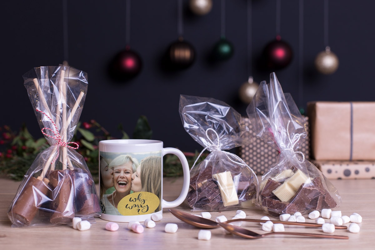 Eine persönliche Fototasse als Teil eines Geschenksets mit Geschenktüten voller Schokolade und Mini-Marshmallows