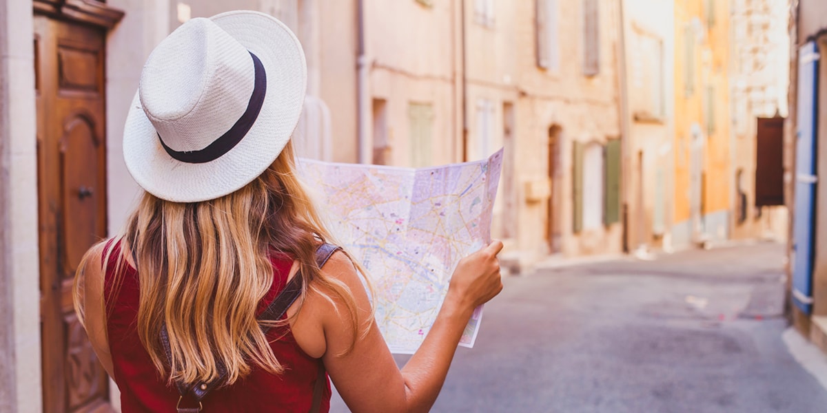 Eine Frau auf einer Städtereise, ihr Rücken zeigt in die Kamera und sie schaut sich eine Karte in einer ruhigen Straße an einem sonnigen Tag an.