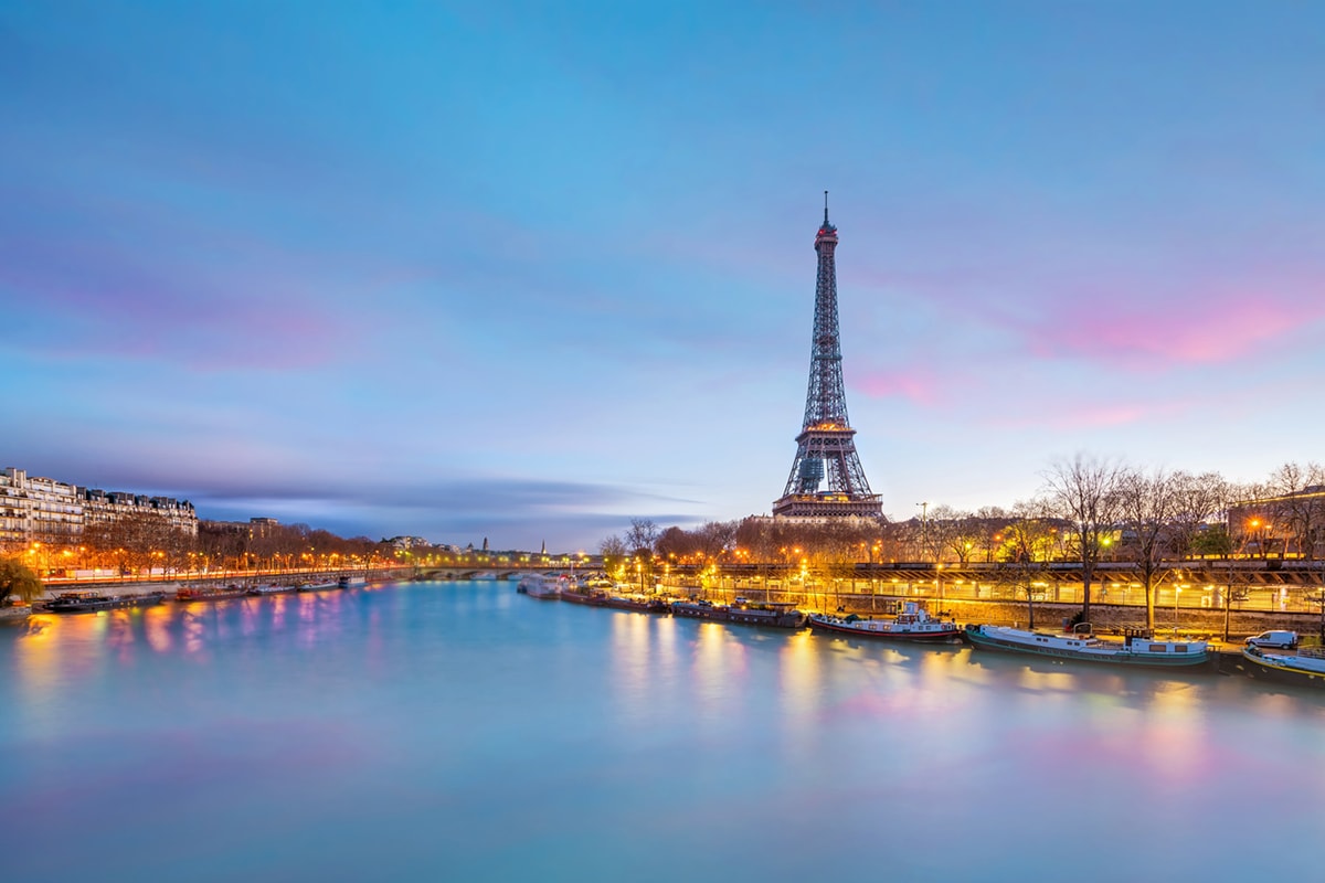 Ein Foto des Eiffelturms, das bei Dämmerung auf der anderen Seite des Flusses aufgenommen wurde.