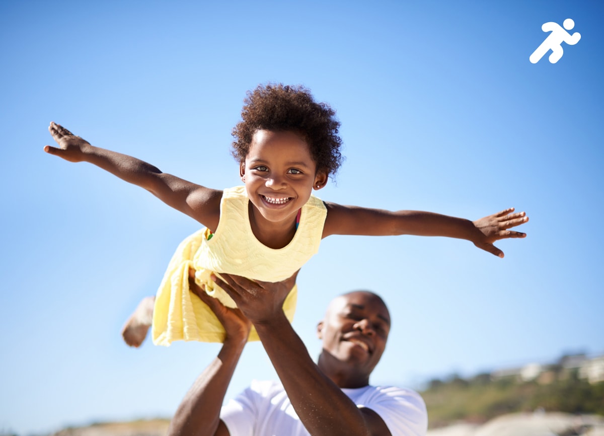 Eine Momentaufnahme eines kleinen Mädchens, das von seinem Vater an einem hellen, sonnigen Tag in die Luft geworfen wird.
