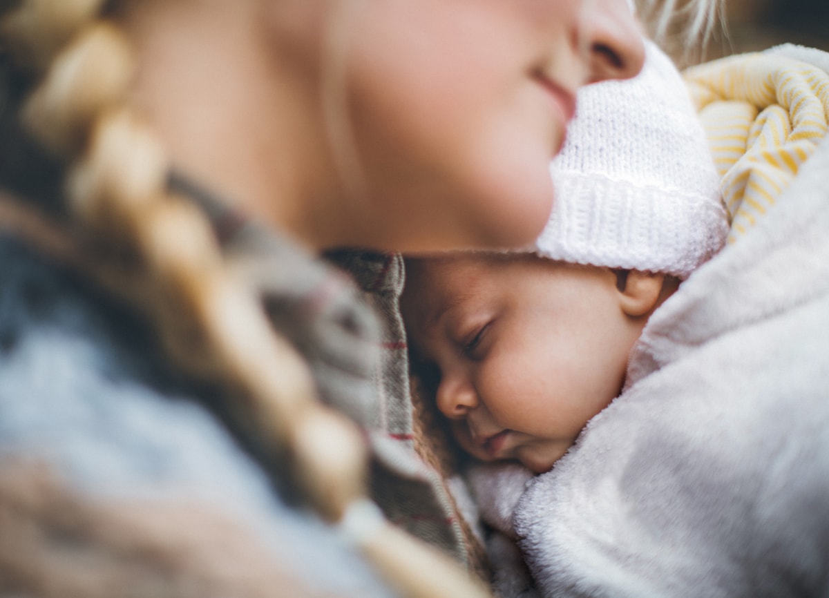 Nahaufnahme einer Frau und eines schlafenden Babys. Die Frau im Vordergrund ist leicht unscharf, während das Baby im Fokus steht.