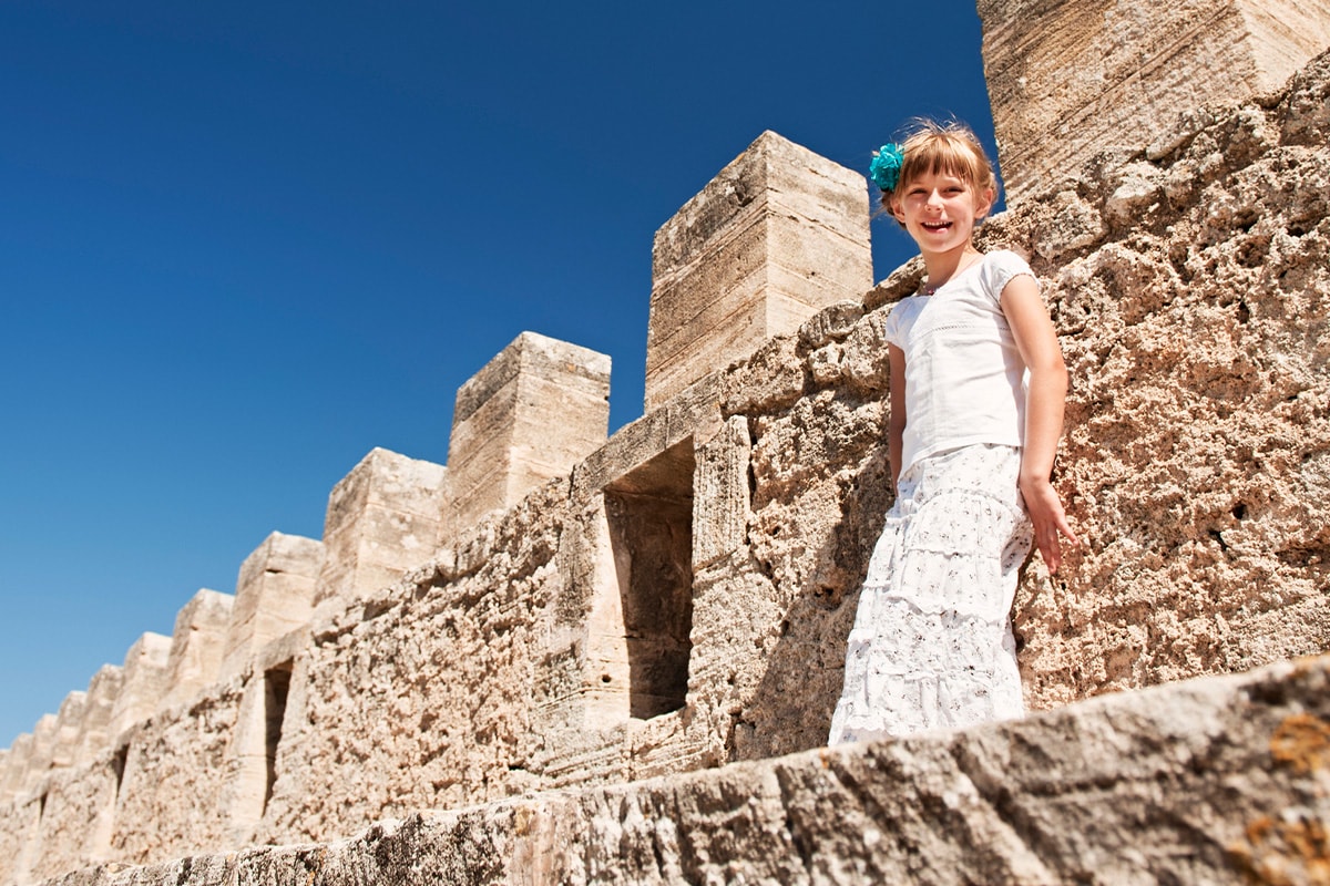 Ein junges Mädchen auf der Mauer einer alten Festung unter einem strahlend blauen Himmel.