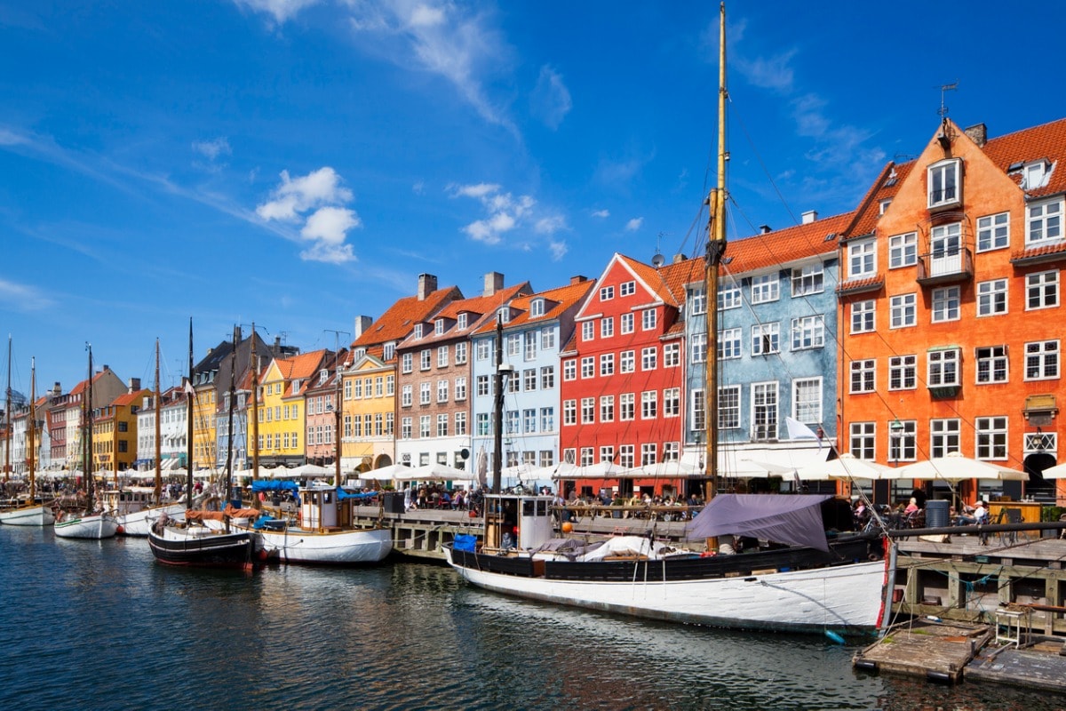 Een foto van de felgekleurde gebouwen in de haven van Kopenhagen, met kleine zeilboten die aan de steiger zijn aangemeerd. 