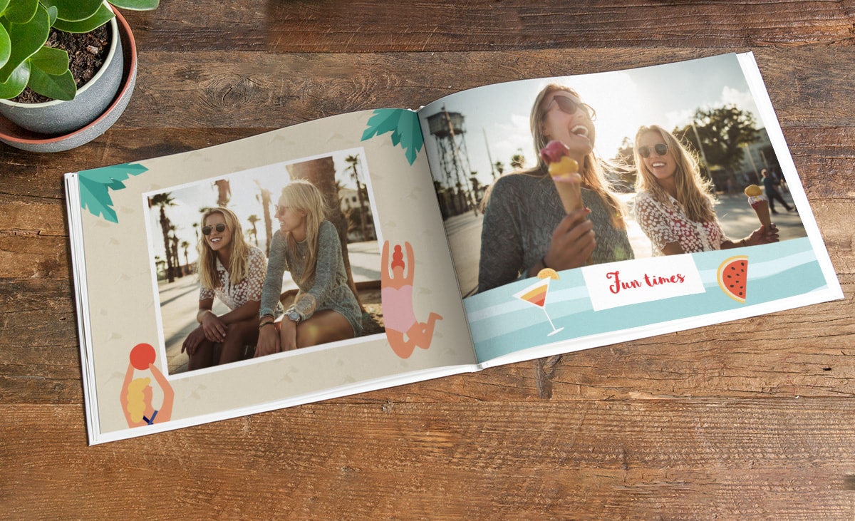 Een opengeslagen fotoboek op een houten tafel. Op beide pagina's zijn zomerse foto's van twee vrienden afgebeeld, die worden omlijst door clipart met een zomerthema, zoals een watermeloen, cocktails, palmbladeren en mensen in zwemkleding. 