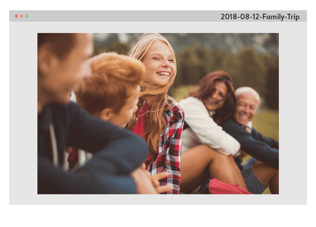 Een foto van een familie, zittend buiten op het gras, lachend. De foto staat in een computervenster, met de bestandsnaam 20180812_Familie_uitje in de hoek rechtsboven.
