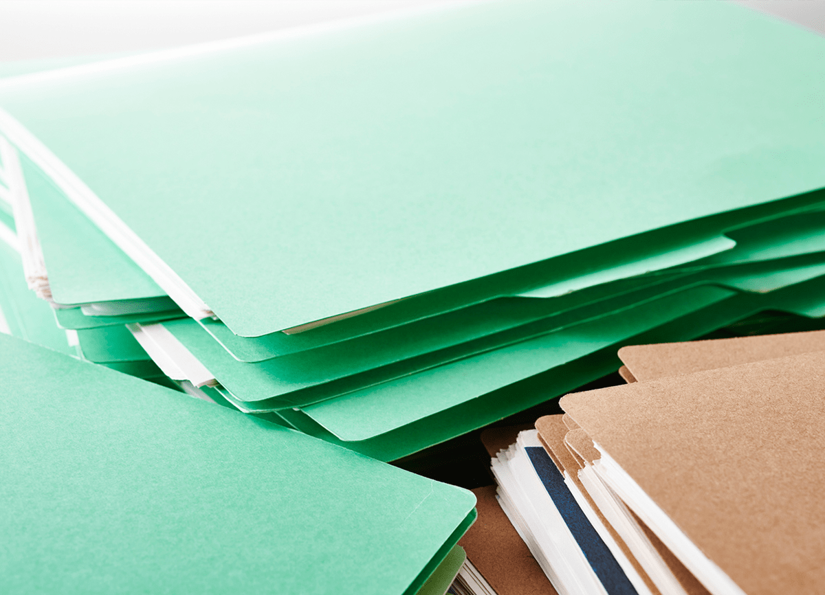 Drie stapels papieren mappen, waarvan twee stapels met groene mappen en eentje met bruine mappen.