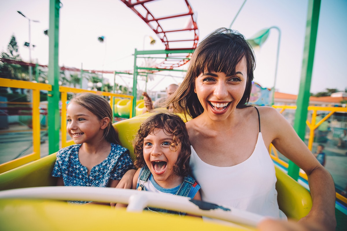 Een vrouw en twee jonge kinderen glimlachend in een achtbaan