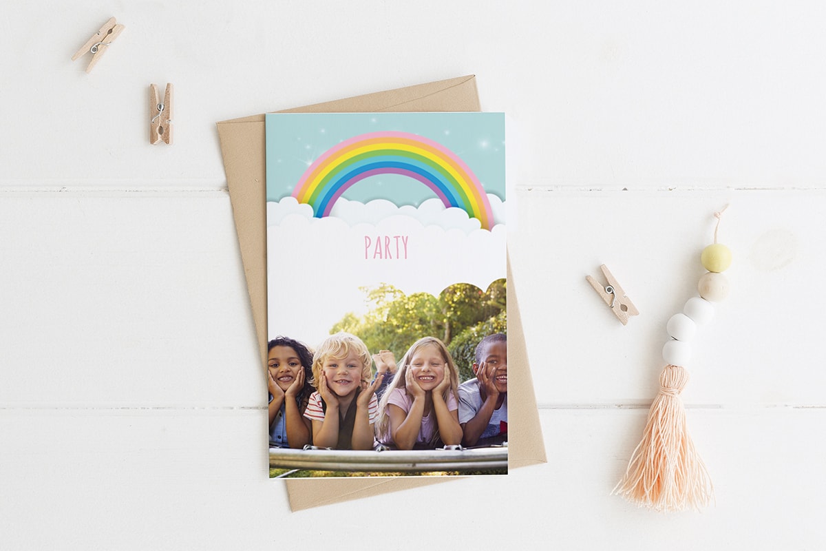 Een verjaardagskaart met een regenboog en een foto van vier kinderen die op het gras liggen.