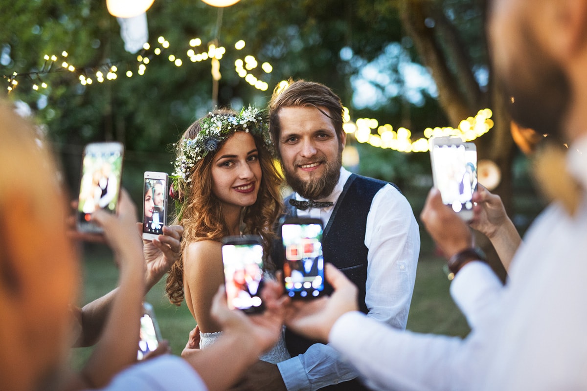 Een foto van een bruid en bruidegom buiten, waarbij alle bruiloftsgasten foto's maken op hun smartphone.