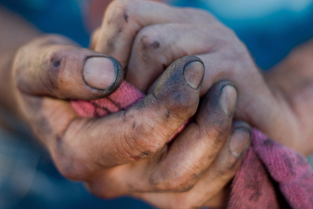 Een close-up foto van een paar mannenhanden, bedekt met aarde, die een doek vasthouden. 
