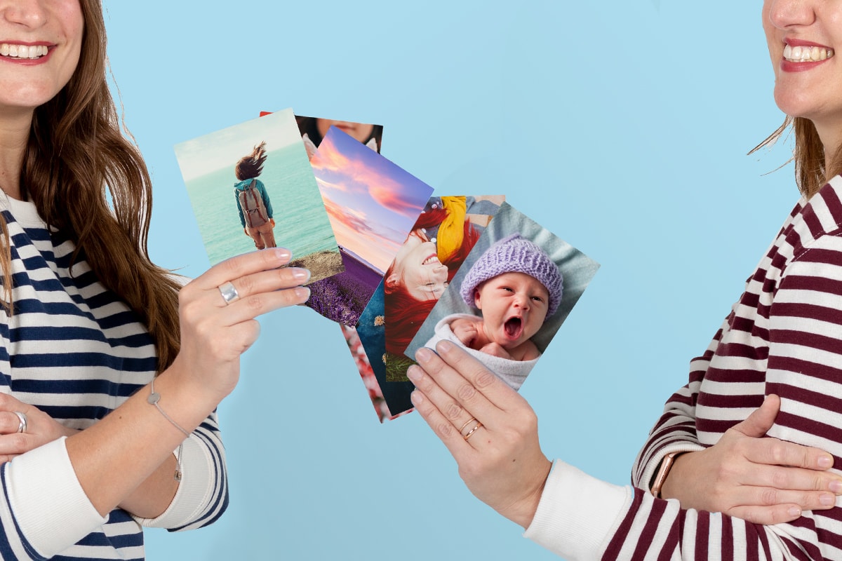 Twee vrouwen met gestreepte topjes, met fotoprints in hun hand. 