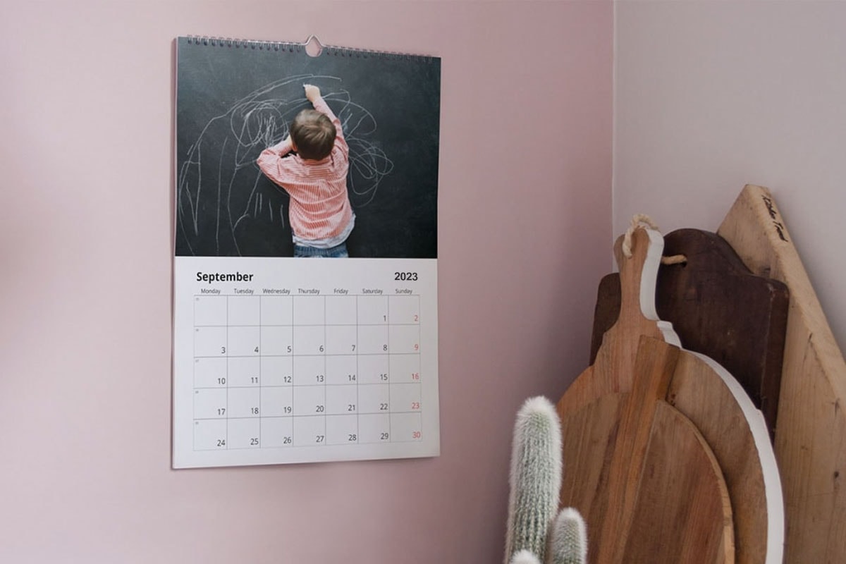 Een foto van een fotokalender tegen een roze muur met een foto van een jongetje dat op een bord aan het tekenen is.