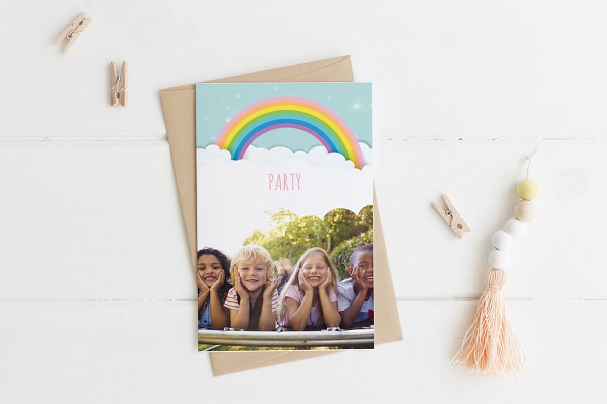 Een verjaardagskaart met een regenboog en een foto van vier kinderen die op het gras liggen.