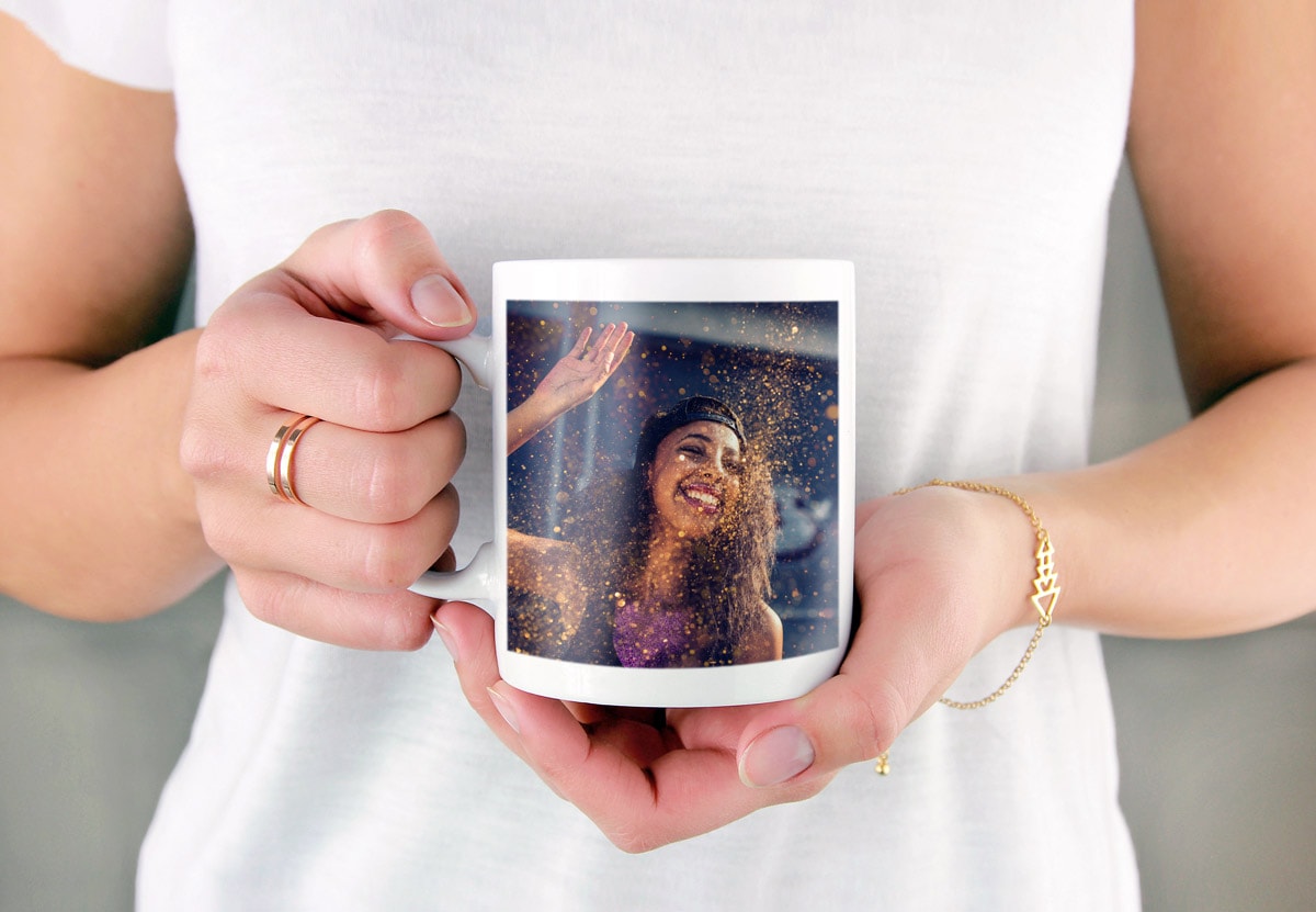 A close-up of a woman holding a photo mug with a picture of a woman at a festival on the side.
