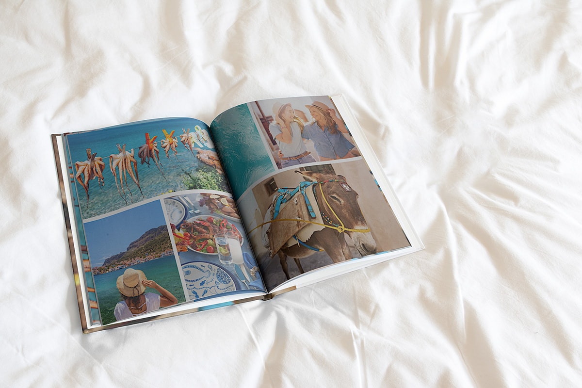 En fotobok ligger öppen på ett vitt påslakan. Ett mosaikcollage av tre bilder finns på båda sidorna och var och en av dem innehåller en semesterbild.