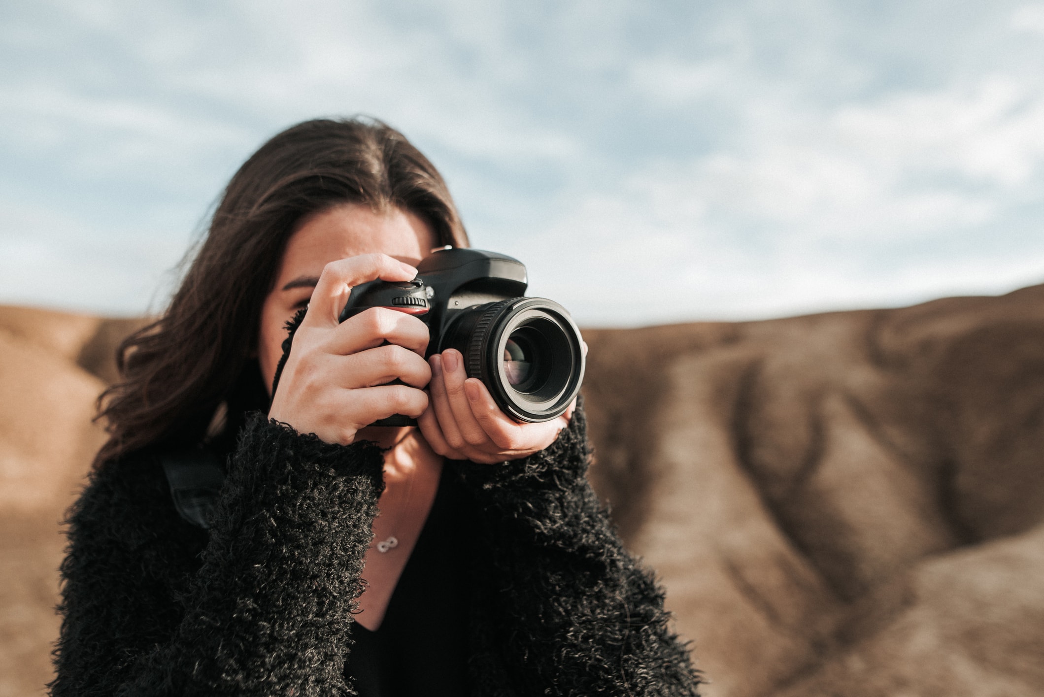 Bild av en tjej som tar ett fotografi med en DSLR-kamera framför en stenig bakgrund