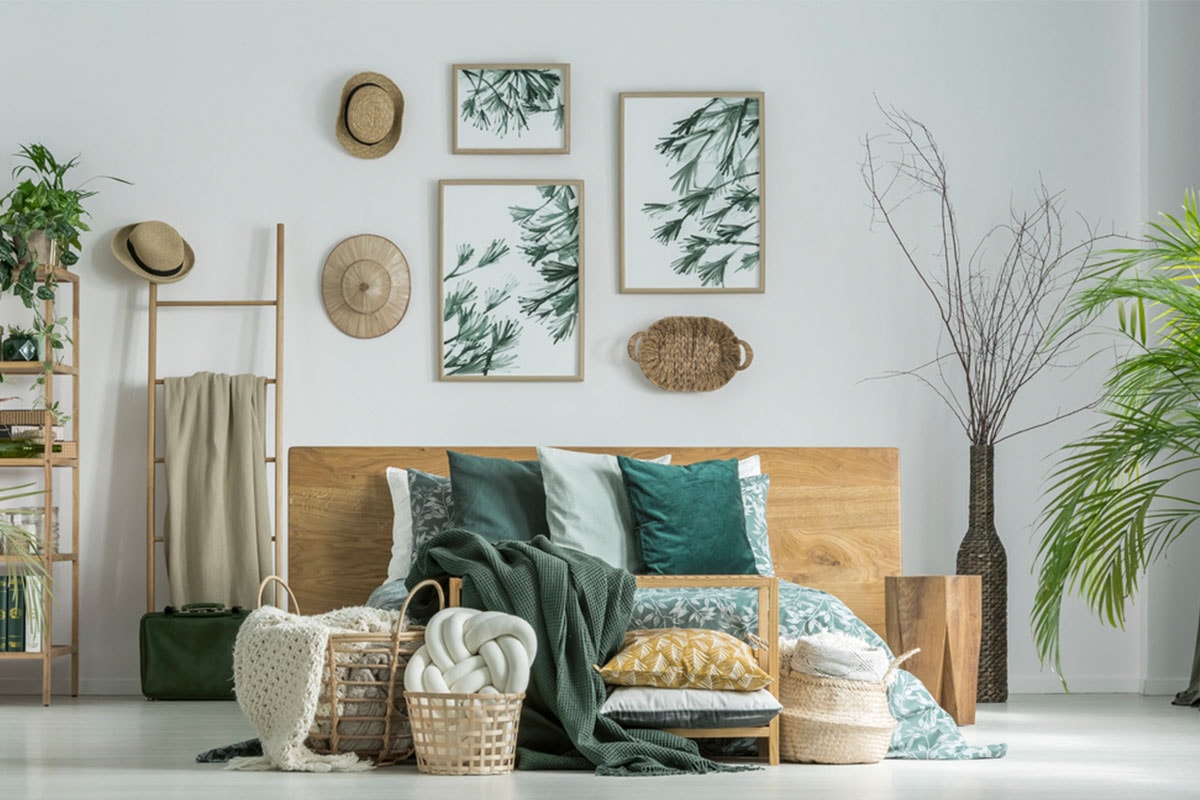 Et soverom med grønne møbler, ulike pynteputer på sengen og interiørprodukter med bladmønstre på veggen bak sengen.