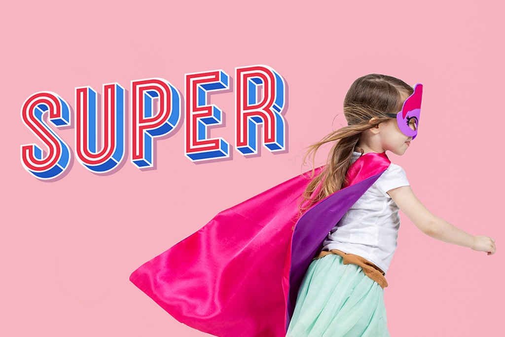 En liten jente på rulleskøyter, kledd som en superhelt i en rosa kappe med ordet ‘super’ i trykkbokstaver på en rosa bakgrunn.