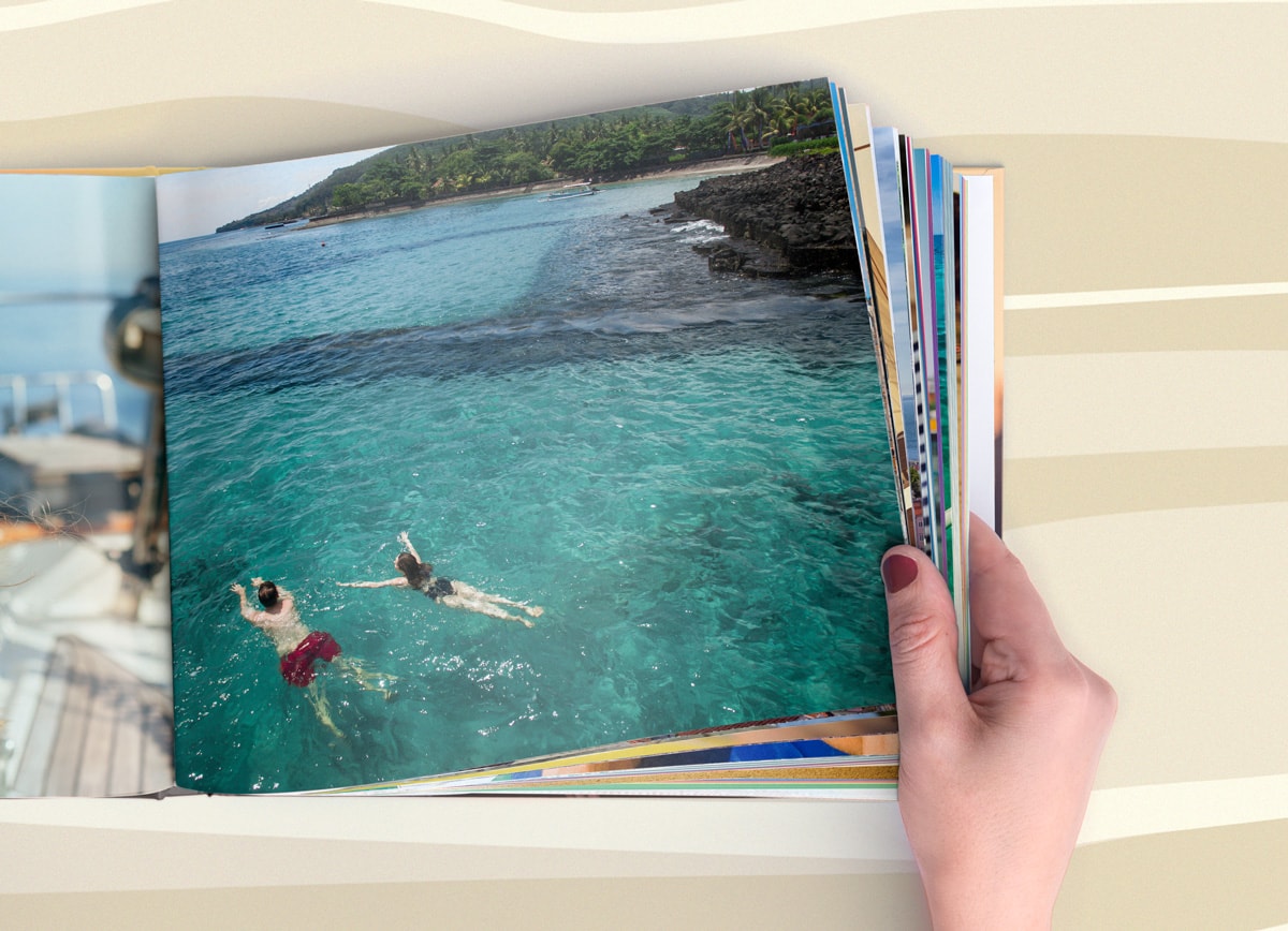 Une main feuilletant un album de photos d'été grâce à une insertion de pages supplémentaires.