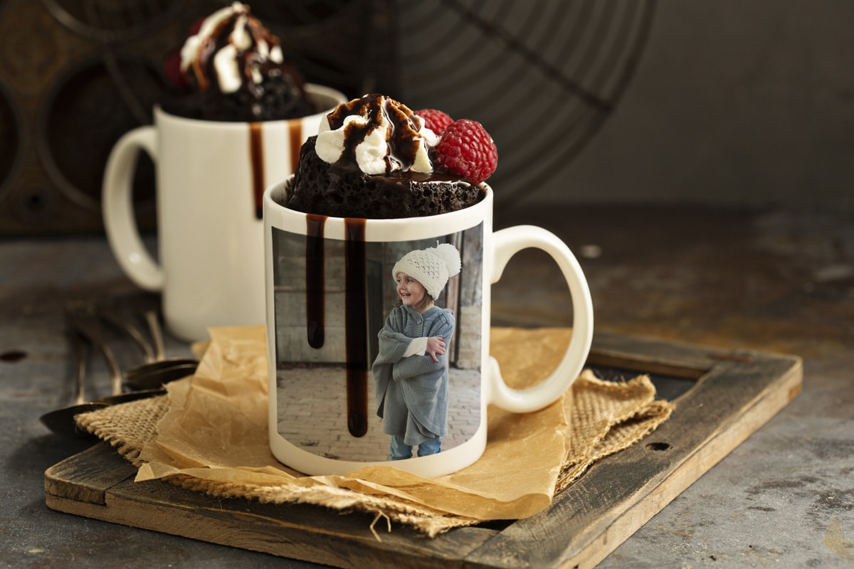 Deux mugs photo ornés d'images hivernales et remplis de mugcakes au chocolat, de crème chantilly et de sauce au chocolat sur le dessus