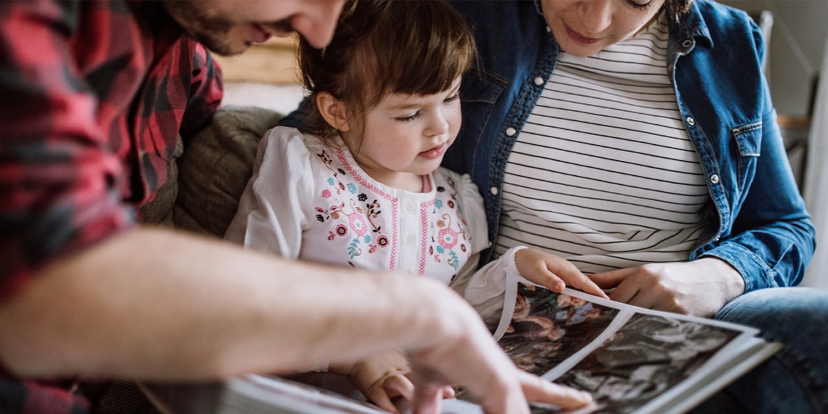 Un homme et une femme assis avec une petite fille, feuilletant un livre photo de famille.