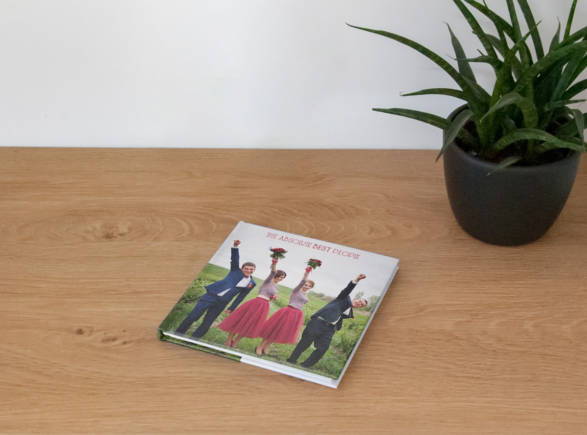 Petit livre photo de mariage carré sur une table en bois avec demoiselles et garçons d'honneur sur la couverture.